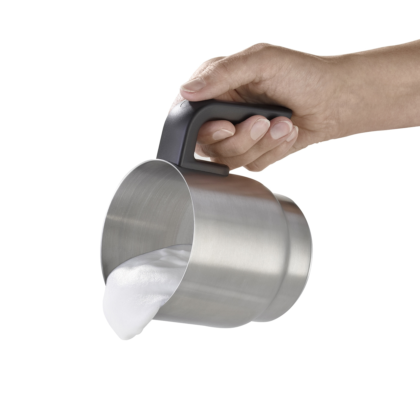 Hand holding metal pitcher with milk foam pouring out, isolated on white background.