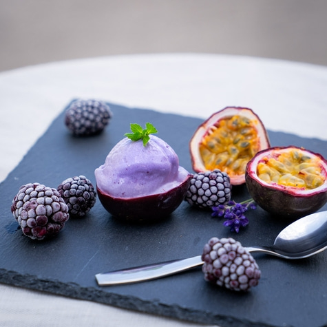 Lila Eiscreme in einer Passionsfrucht mit Brombeeren und Minze auf einem schwarzen Brett
