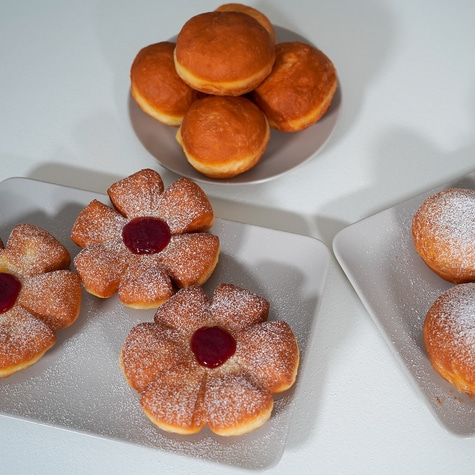 Flower and round donuts with powdered sugar and jam on plates
