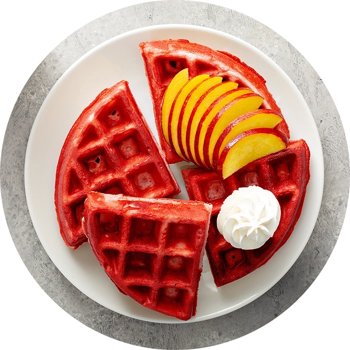 Rote Waffeln mit Pfirsich und Sahne auf einem weißen Teller