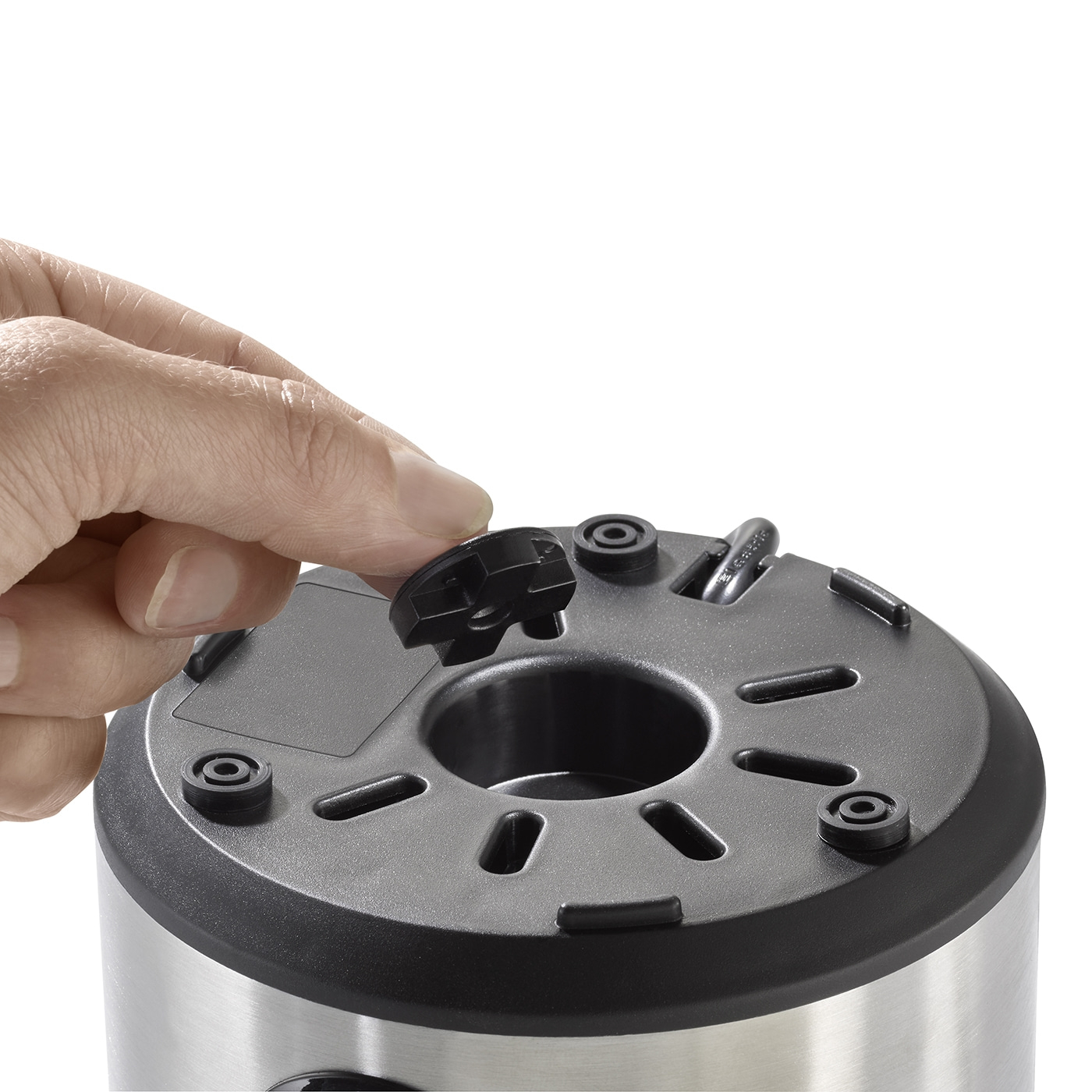 Hand holding black part over silver device with holes and buttons.