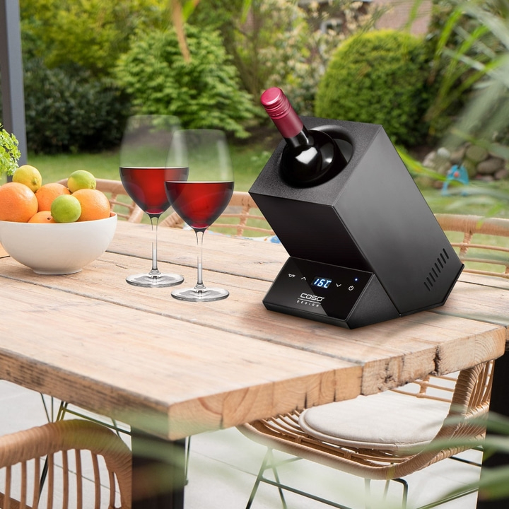 Wine bottle cooler with two wine glasses and fruit on a wooden table outdoors
