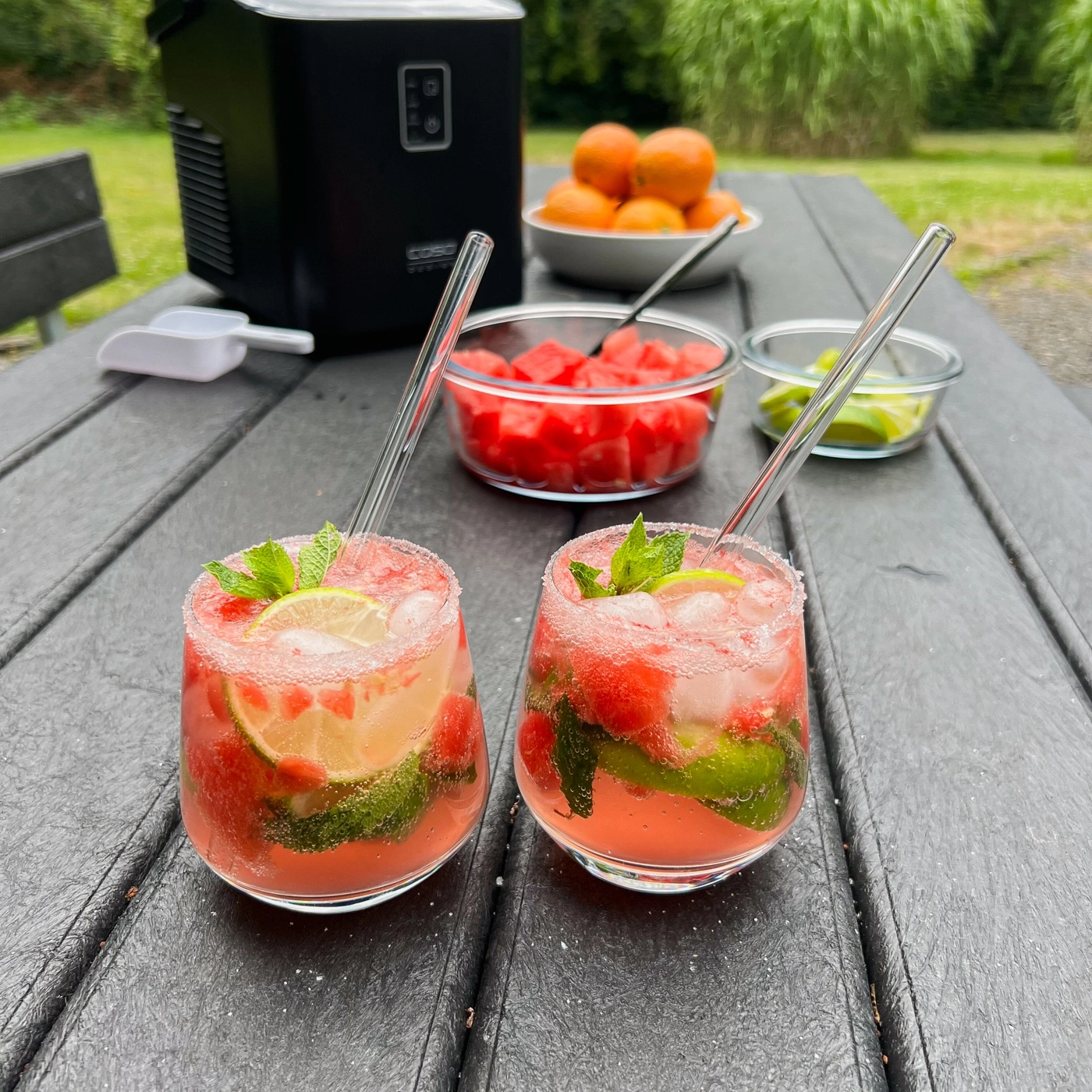 Zwei Cocktails mit Wassermelone, Limette und Minze auf einem Tisch mit Eiswürfeln.