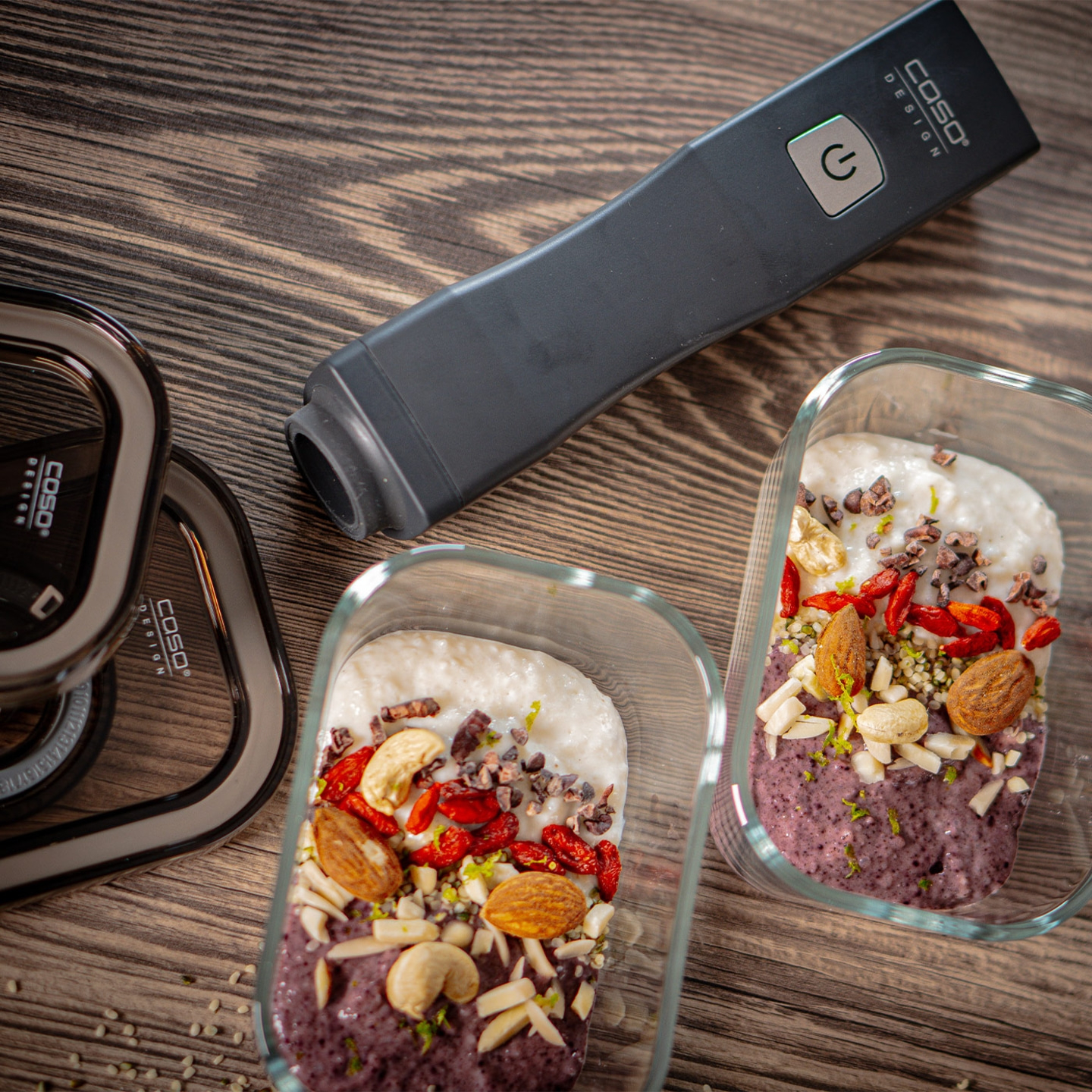 Two glass containers of food, next to a vacuum sealer on a wooden table.