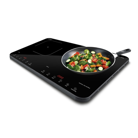 Induction cooktop with vegetable pan, black surface, digital display, cooking.