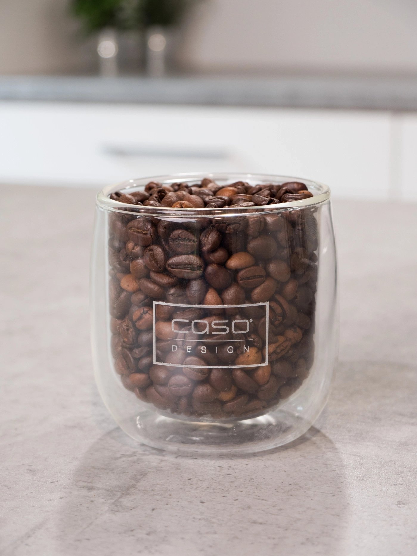Ein Glas mit gerösteten Kaffeebohnen und dem CASO Design-Logo.