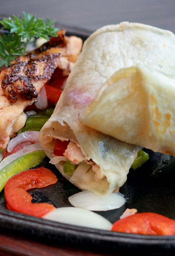 Close-up of a chicken and vegetable burrito on a plate with ingredients