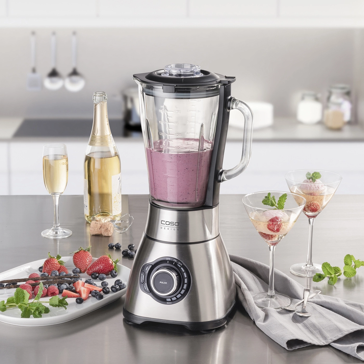 Blender with fruits, drinks and ingredients on a kitchen countertop setting.