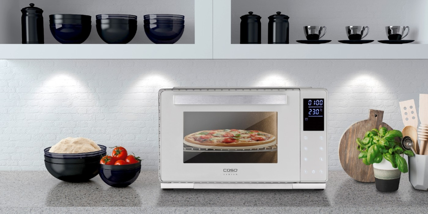 Pizza oven with pizza, ingredients, and kitchen utensils on a countertop.