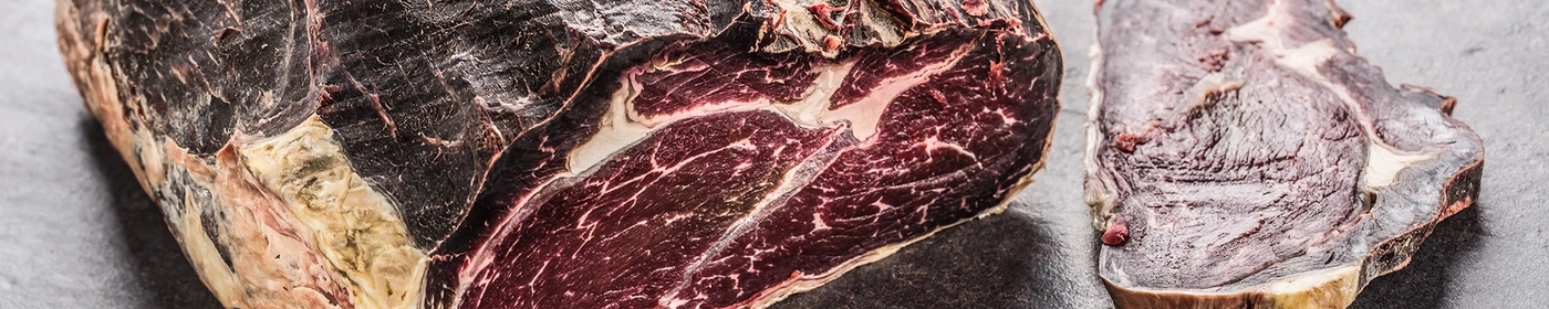 Two pieces of dry-aged beef, showing marbling and a dark, aged crust.