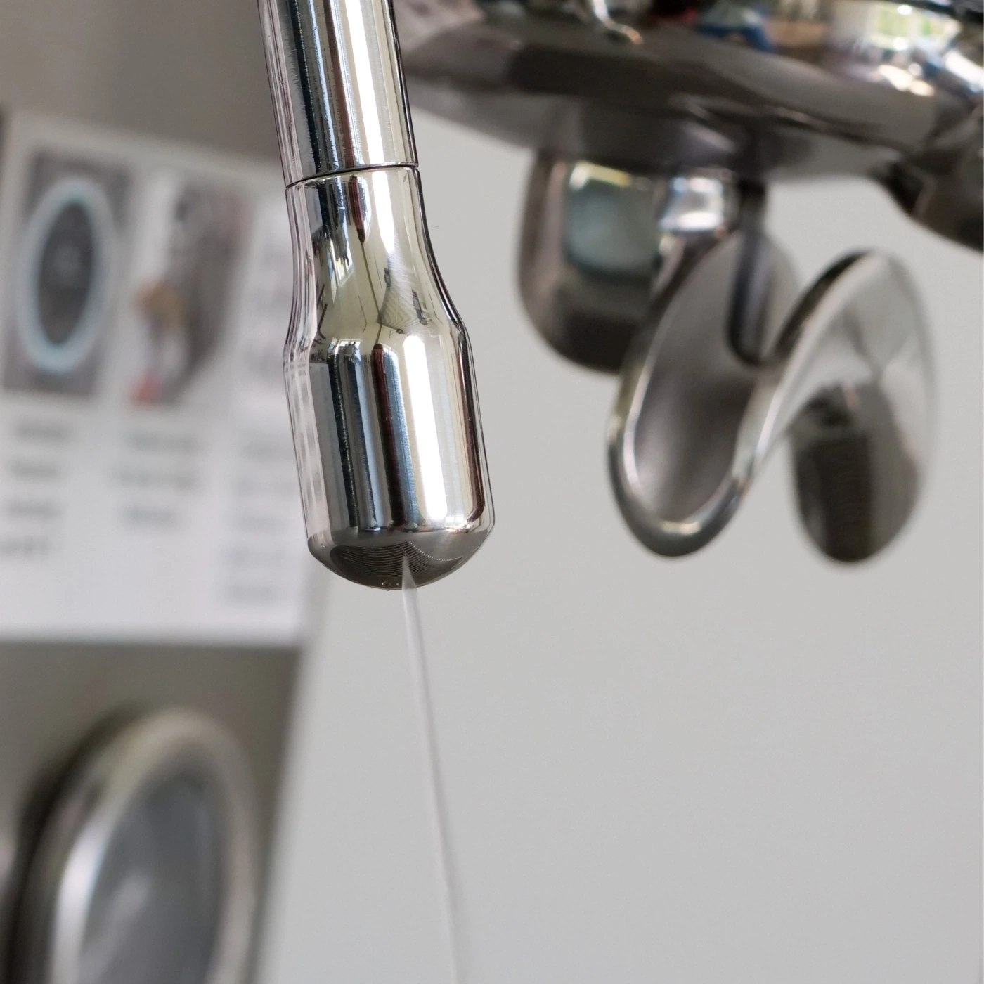 Nahaufnahme von Wasser, das aus einem Chromwasserhahn tropft, mit verschwommenem Hintergrund von Waschmaschinen.