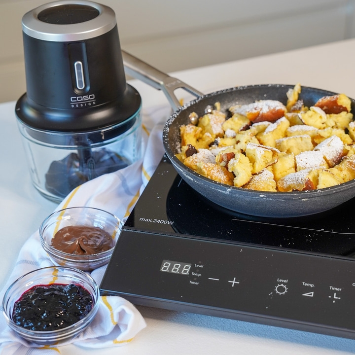 Pancakes with powdered sugar, blueberries, chocolate cream, and a Caso design mixer on a cooktop.