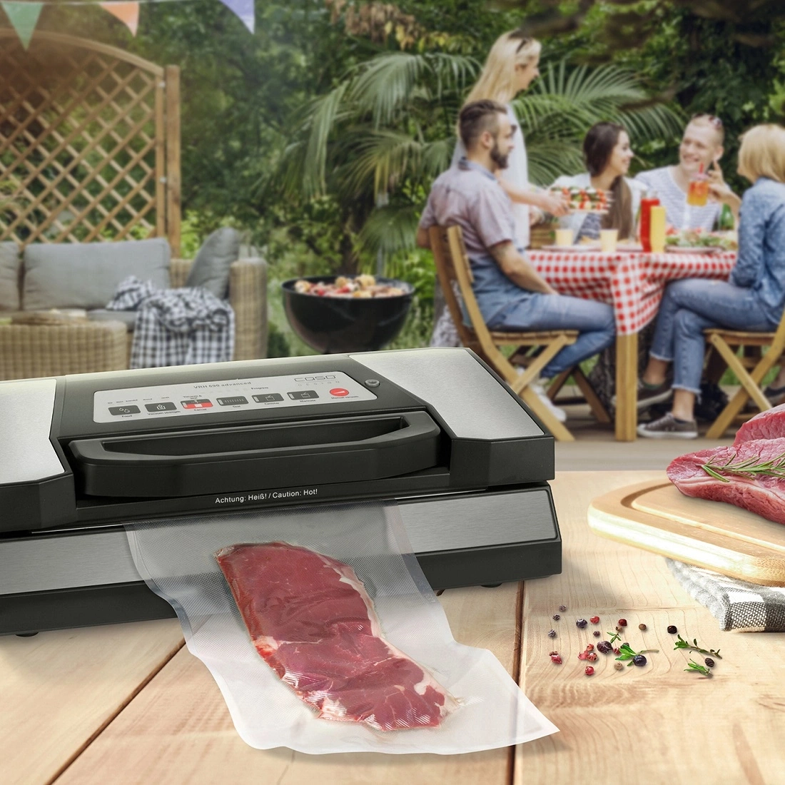 Vakuumiergerät mit Fleisch, Grillparty im Hintergrund, Holzoberfläche, Essen