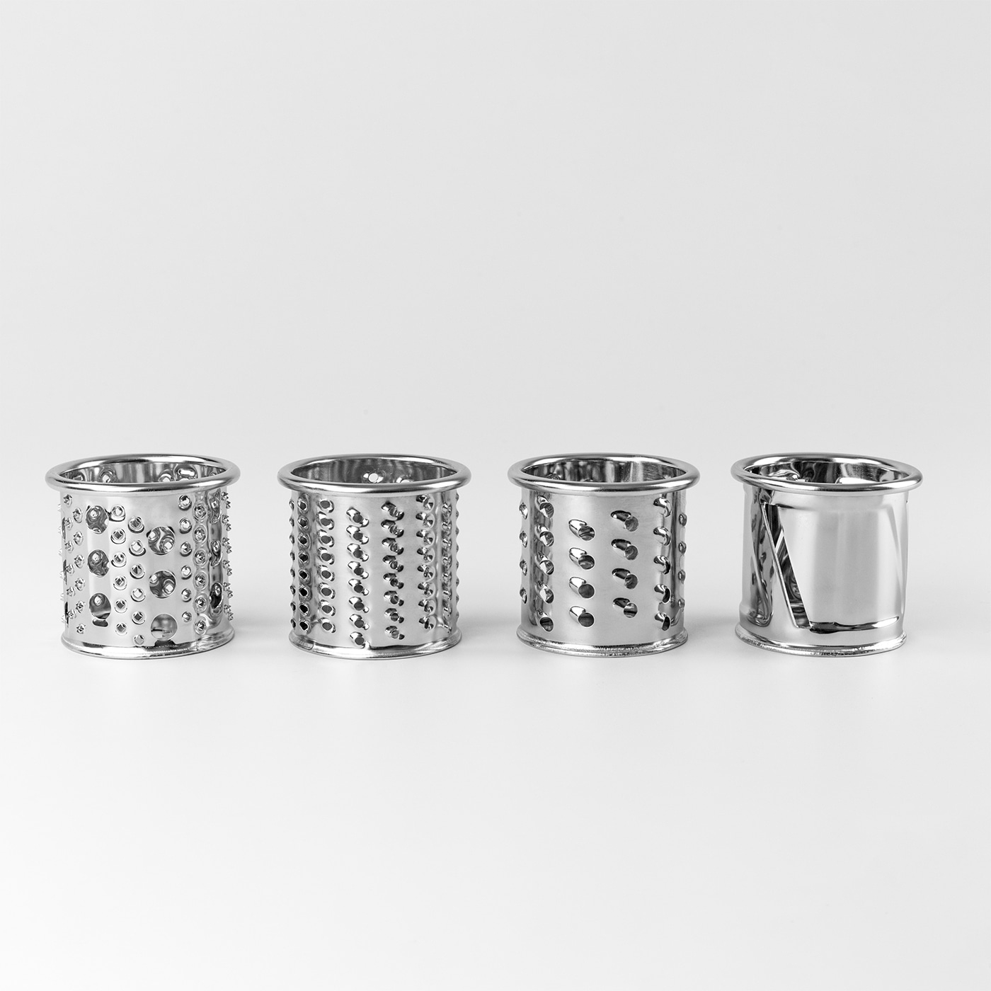Four metal graters standing on a white surface, kitchen tools for food preparation.
