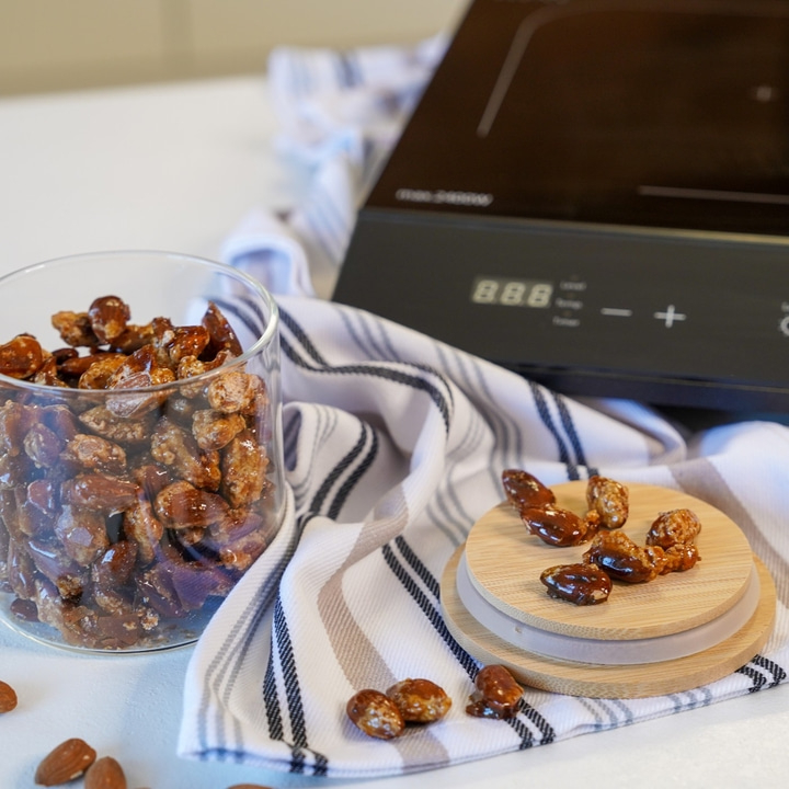 Glass of candied almonds, wooden lid, stovetop, striped cloth, close-up shot