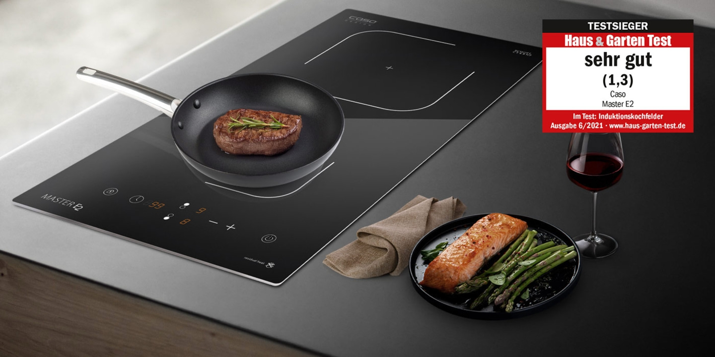Induction cooktop with steak, salmon, asparagus, wine, and award.