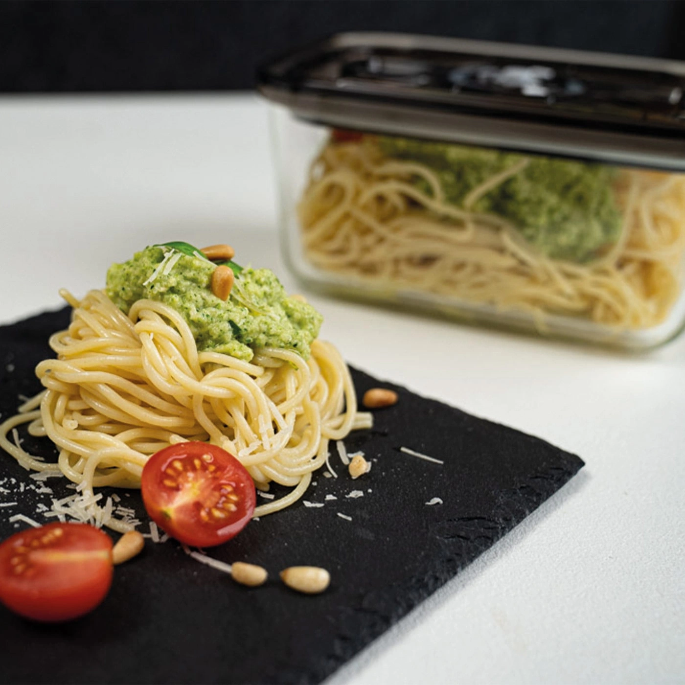 Spaghetti with pesto, tomatoes, and pine nuts served on a black slate.