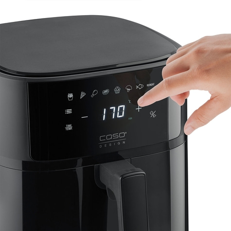 Black air fryer with digital display and hand pressing a button on the device.