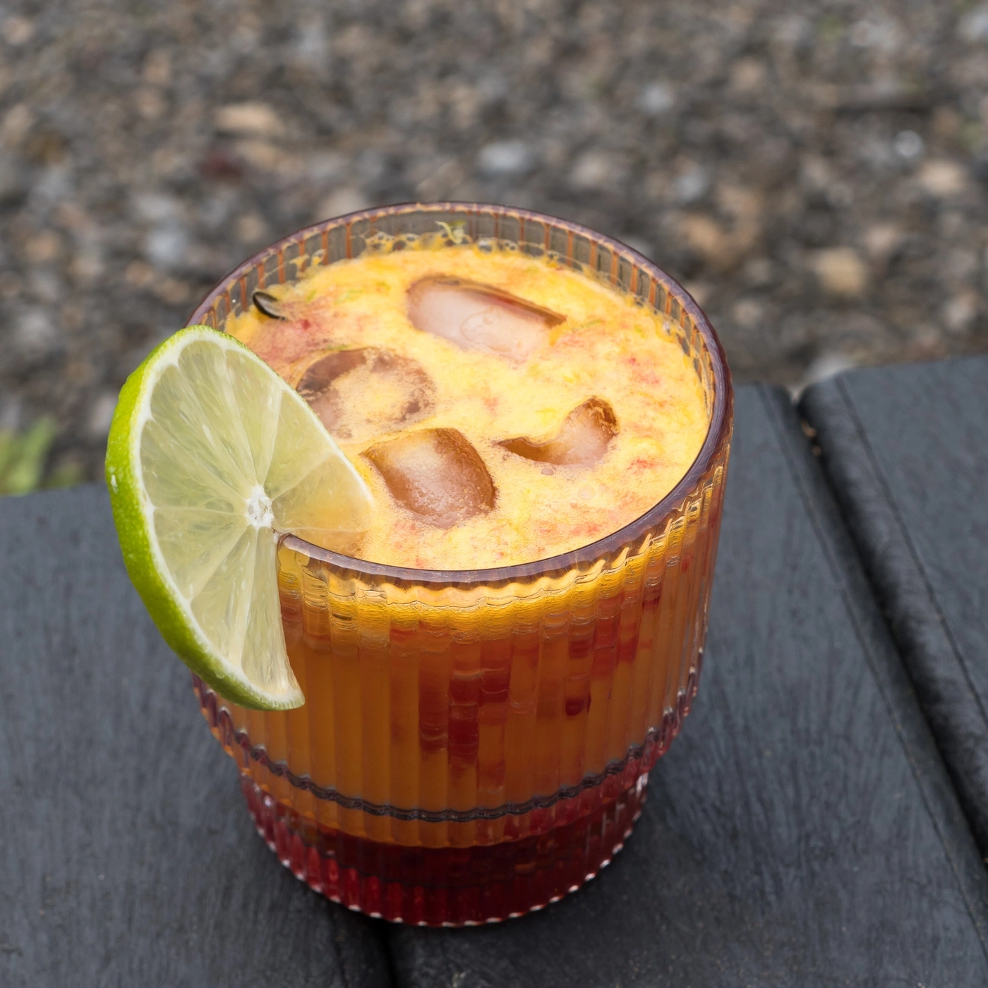 A glass of orange drink with ice cubes and a lime wedge garnish.