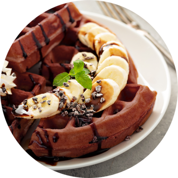 Chocolate waffles with bananas, chocolate sauce, and mint on a plate