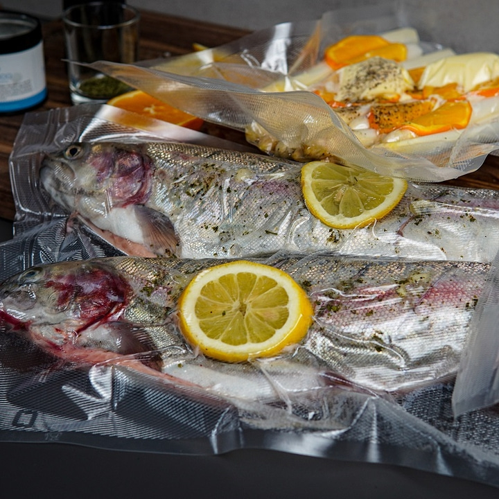 Two fish in vacuum bags with lemons and oranges, ready for cooking.