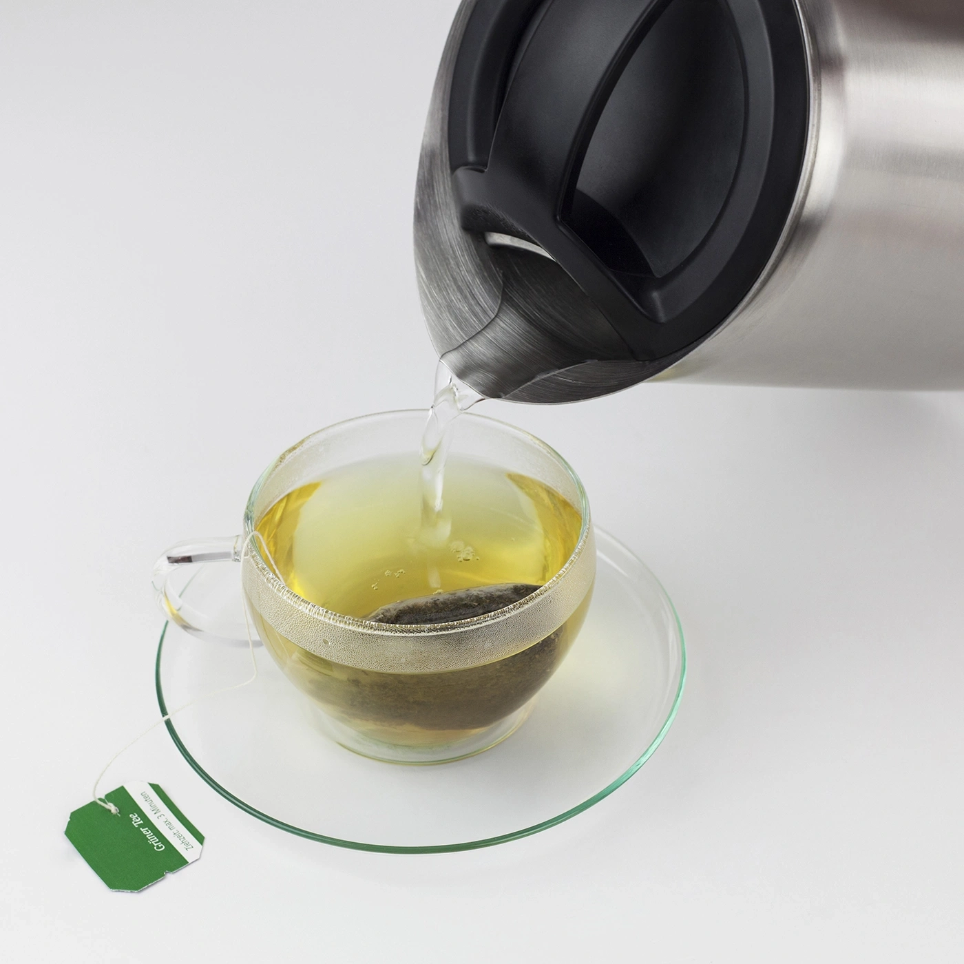 Hot water pouring into teacup with tea bag, close-up, white background, tea time.