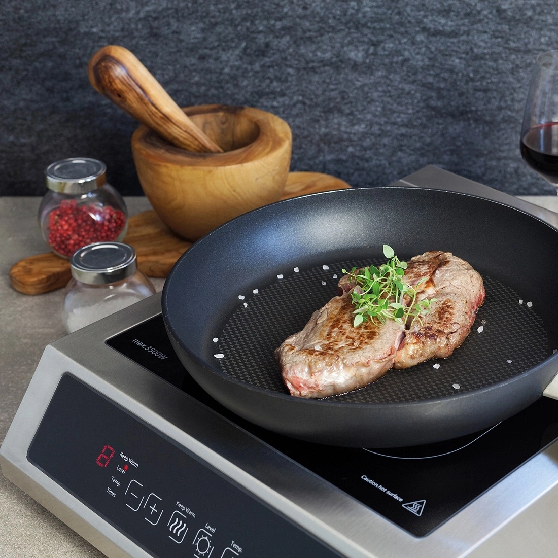 Steak cooking on induction cooktop with herbs and salt in a pan, ready to eat.