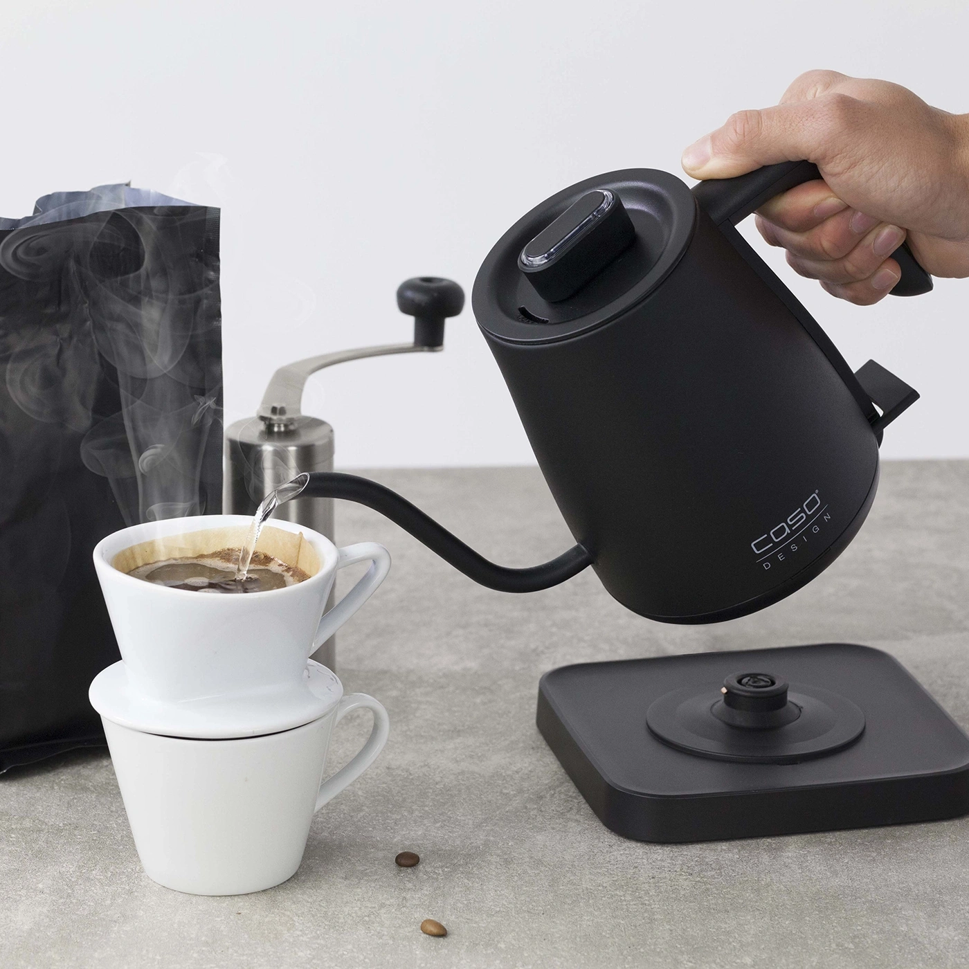 Kaffeekanne gießt Wasser in eine Tasse. Kaffeemühle und Kaffeebohnen.