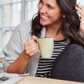 Smiling woman holding a coffee mug, relaxing. Happy, enjoying a moment.