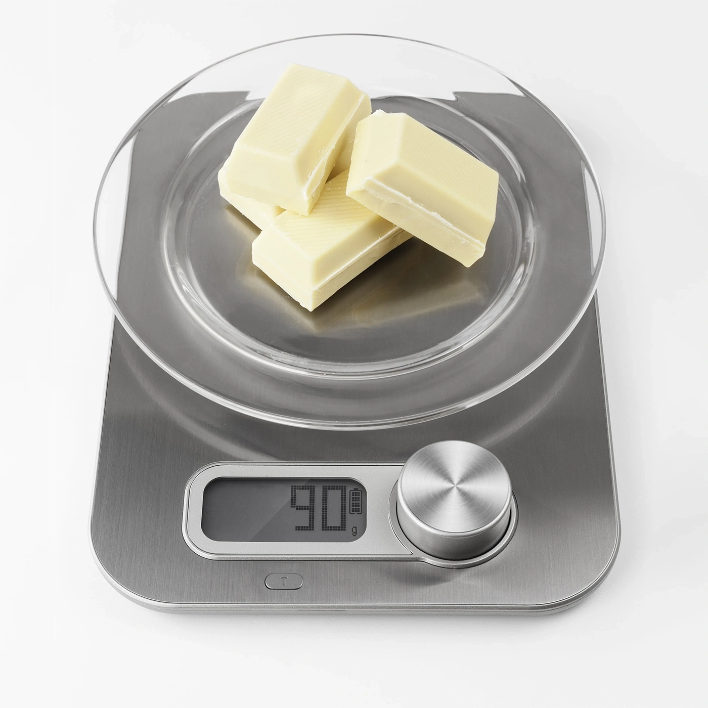 Scale with chocolate, showing 90g, on a glass plate, silver color.