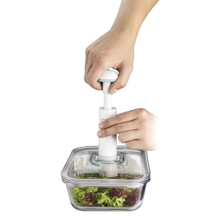 Person vacuuming salad in glass container with pump, close-up shot