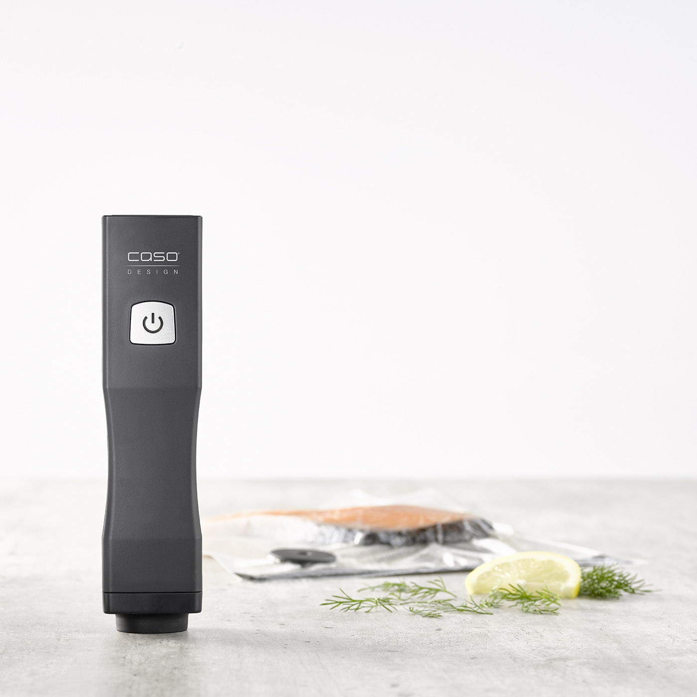 Vacuum sealer with lemon, dill, and fish in foil on a gray surface