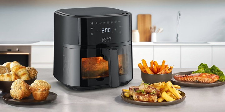 Black air fryer with food being prepared on a table in a kitchen setting.