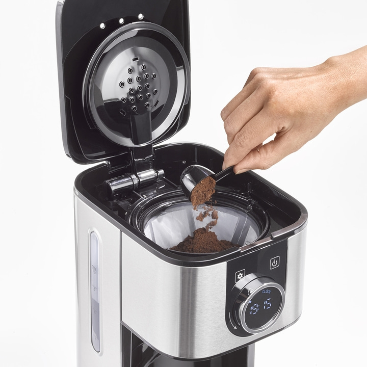 Kaffeemaschine wird mit Kaffeepulver befüllt. Hand mit Löffel. Kaffeezubereitung.