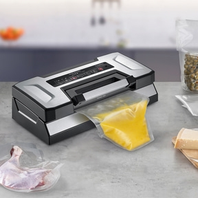 Vacuum sealer with food: meat, cheese, olives, and yellow liquid in a bag.