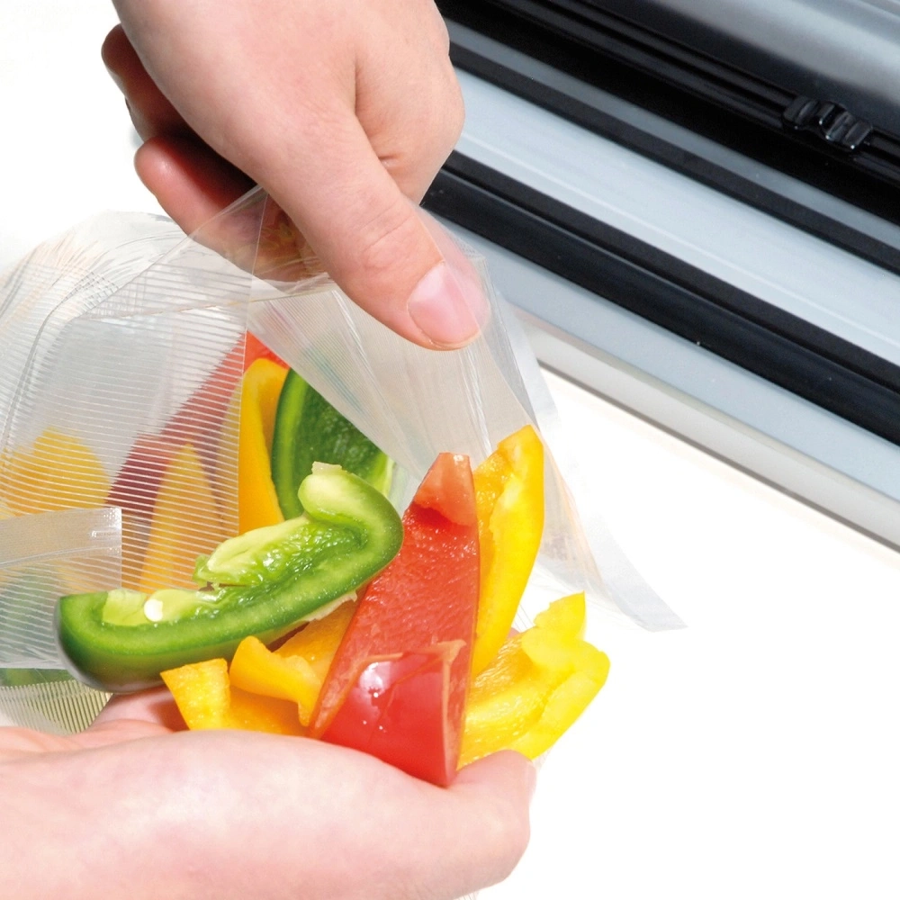 Person holding a bag of peppers in front of a vacuum sealing machine.