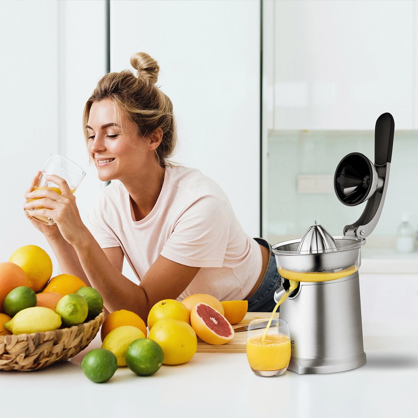 Woman drinking fresh juice next to a citrus juicer and fruit in the background.