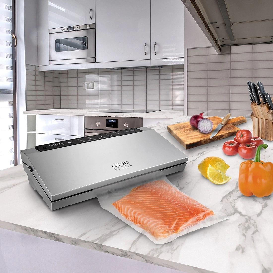Kitchen with vacuum sealer, salmon, vegetables, and utensils on marble surface.
