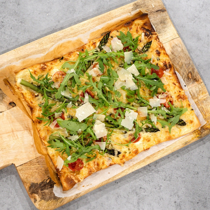 Rectangular pizza with arugula, asparagus, and cheese on a wooden board