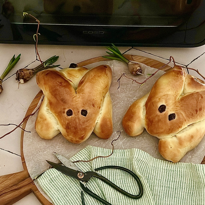 Zwei Hasenbrote auf einem Holzbrett mit Schere und Dekoration.