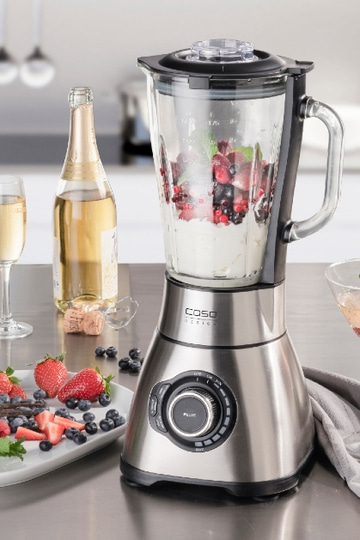 Edelstahl-Mixer mit Früchten, Champagner und Erdbeeren auf einem Tisch
