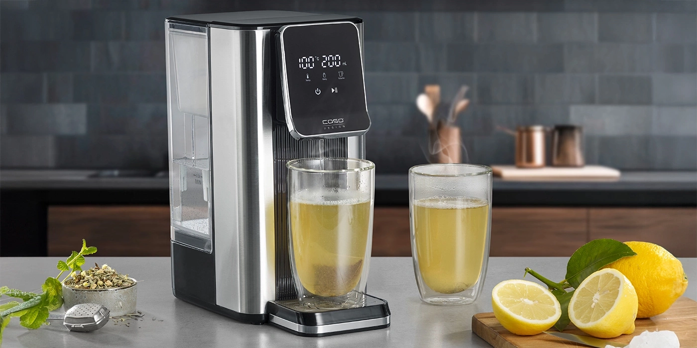 Teemaschine mit zwei Gläsern Tee und Zitronen auf einem Schneidebrett.