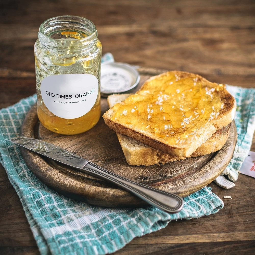 Marmelade auf Toast mit Messer und Glas auf Holzbrett und Tuch