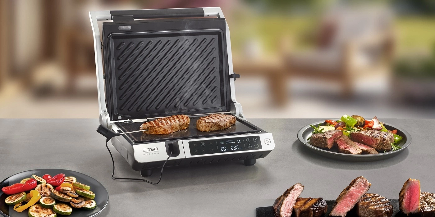 Elektrischer Grill mit Steaks und Gemüse auf dem Tisch