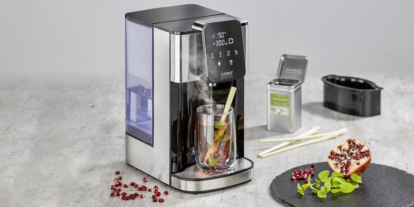 Teemaschine mit Glas, Lemongras, Granatapfel und Kräutern auf einem Steinbrett