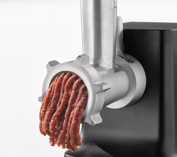 Nahaufnahme eines Fleischwolfs, der Fleisch ausgibt, mit weißem Hintergrund.