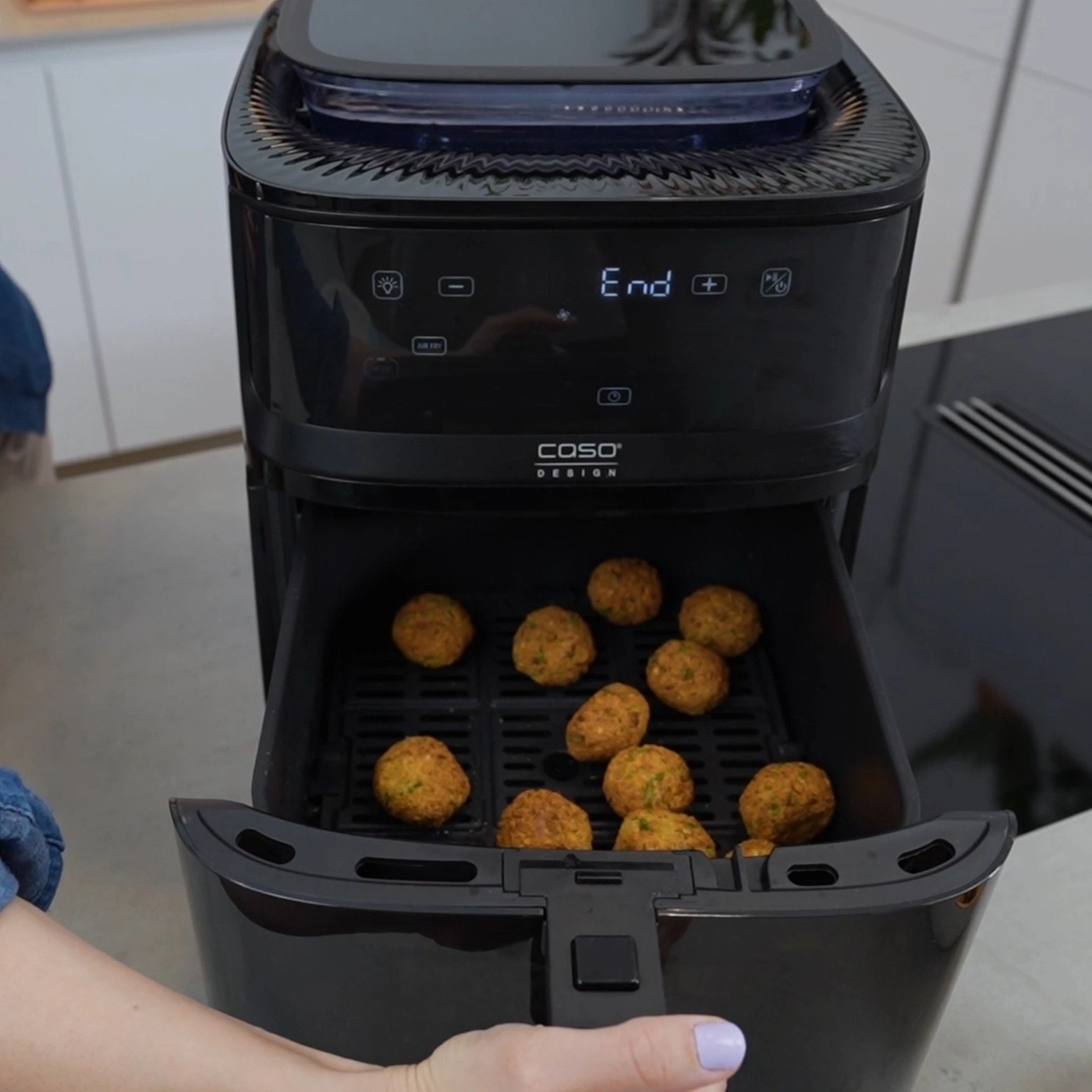 A person opens an air fryer containing falafel.