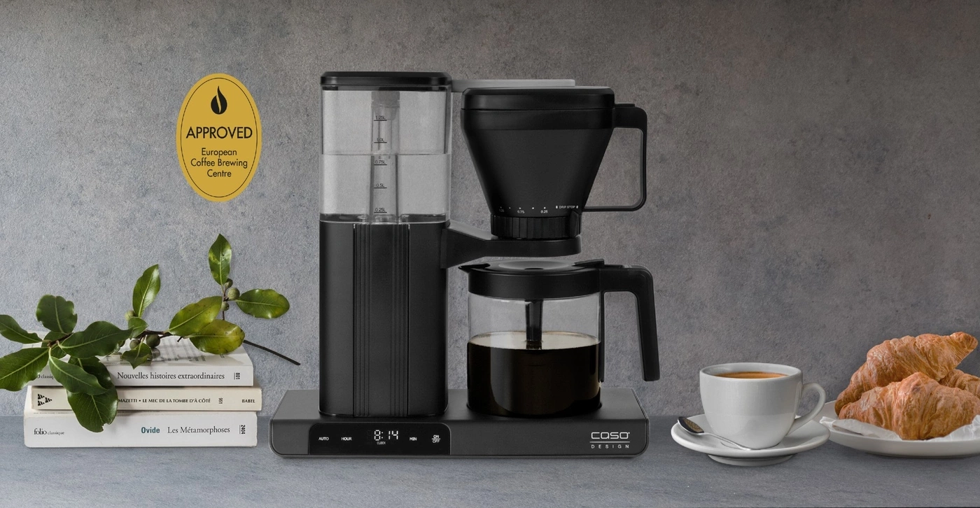 Kaffeemaschine mit Kaffee, Tasse, Croissants und Büchern auf einem Tisch.
