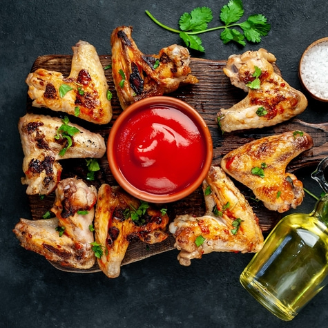 Grilled chicken wings with sauce, oil, and salt on a wooden board.