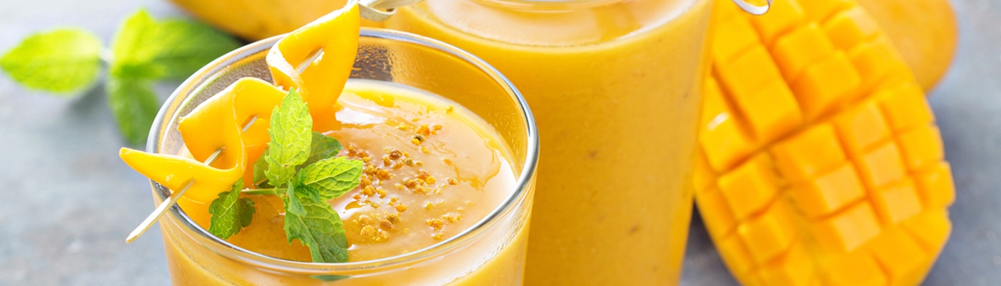 A glass of mango smoothie with mint and mango decoration, next to a glass and a mango.